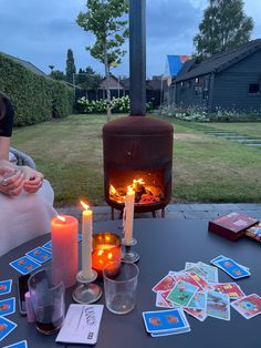 a table topped with candles and cards next to a fire place on top of a lawn