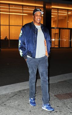 a man standing in front of a building wearing a blue jacket and white t - shirt