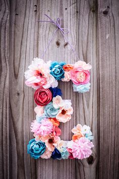 the letter d made out of flowers is hanging on a wooden fence with string attached to it