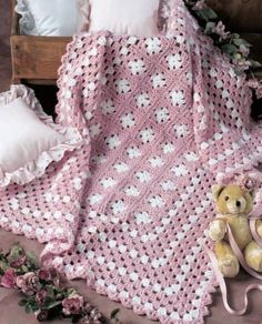 a pink crocheted blanket with white flowers on it next to a teddy bear