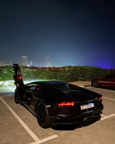 a black sports car parked in a parking lot at night with the city lights behind it