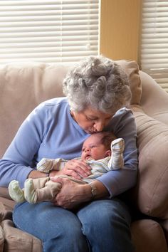 an older woman sitting on a couch holding a baby