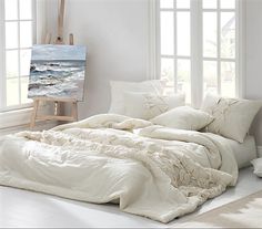 a white bed sitting in a bedroom next to two windows and a painting on the wall