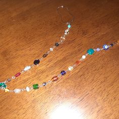 a wooden table topped with a long necklace on it's side and a pair of scissors