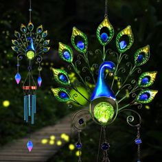 three colorful wind chimes hanging from strings in front of green trees and bushes with lights on them