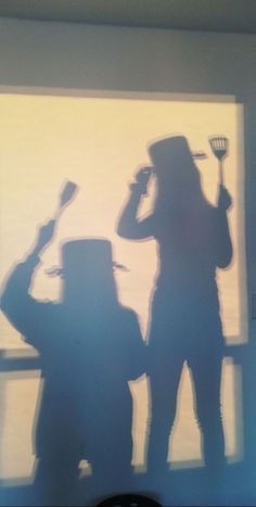 two people standing next to each other in front of a window with shadows on the wall