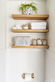 two wooden shelves above a toilet with towels and other items on them in a bathroom