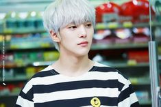 a young man with white hair wearing a black and white striped shirt standing in front of a store