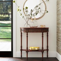 a vase with flowers on top of a wooden table in front of a wall mounted mirror