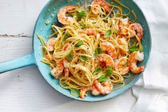 pasta with shrimp and spinach in a blue skillet on a white wooden table