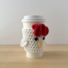 a white coffee cup with a red rooster on it's head and a crocheted lid