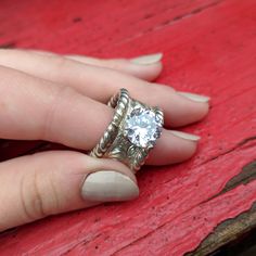 a woman's hand holding an engagement ring on top of a red wooden table