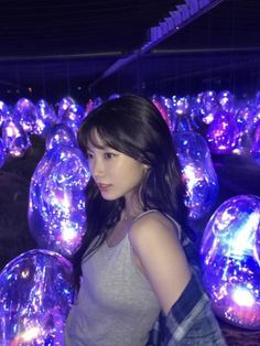 a young woman standing in front of some shiny balls and looking at the camera with an intense look on her face