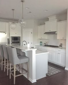 a large kitchen with white cabinets and gray bar stools in front of an island