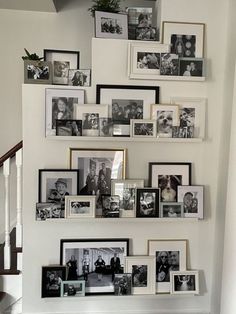 a bunch of pictures are hanging on the wall with frames above them and below it is a staircase