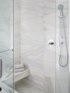 a bathroom with a glass shower door and white marble wallpaper on the walls, along with a bench