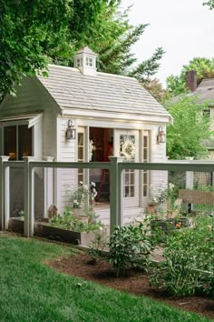 a small white house with a fence around it's perimeter and plants in the yard