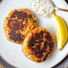 two crab cakes on a plate with a side of sour cream and a lemon wedge