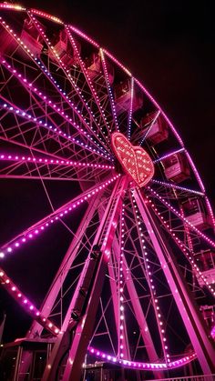 a ferris wheel lit up at night with lights on it's sides and hearts in the center