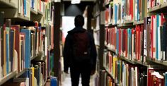 a man is walking down the aisle of a library with many bookshelves full of books