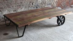 a wooden table sitting on top of a black metal carton next to a brick wall