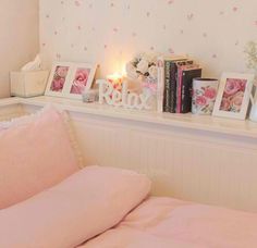 a bed with pink sheets and pillows next to a shelf filled with pictures on it