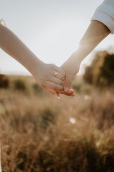 two people holding hands in the middle of a field