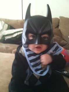 a baby dressed up as batman sitting on a couch