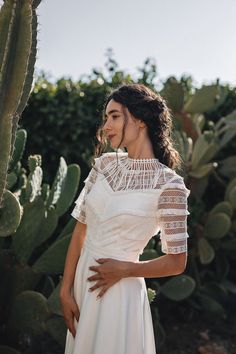 a woman standing in front of a cactus wearing a white wedding dress with sheer sleeves