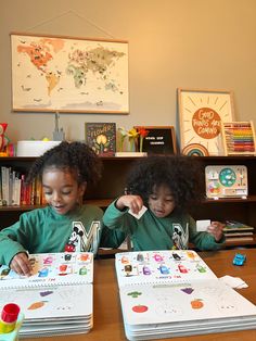 two young children sitting at a table with books and magnets on the desk in front of them