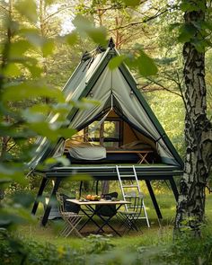 a tent in the woods with a table and chairs under it, surrounded by trees