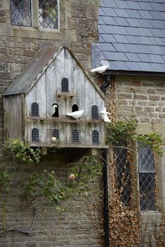 a bird house with several birds perched on it's roof and windows, in front of an old brick building