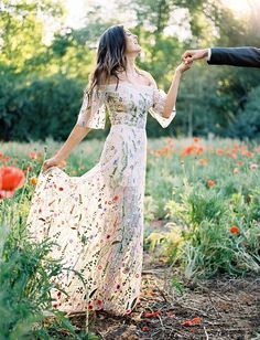 a man and woman holding hands while standing in a field full of red poppies