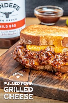 a pulled pork grilled cheese sandwich sitting on top of a cutting board next to a jar of bbq sauce