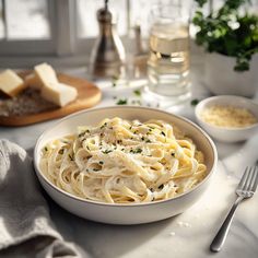 a bowl of pasta with parmesan cheese and bread on the table next to it