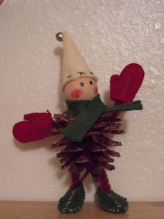 an elf doll holding two red hearts on top of a wooden table next to a white wall