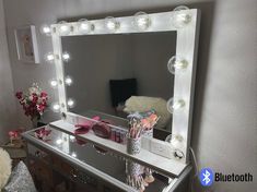 a vanity mirror with lights on top of it and a teddy bear in the background