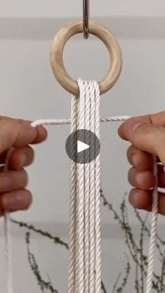 two hands are pulling rope from a hanging planter with a wooden ring on it