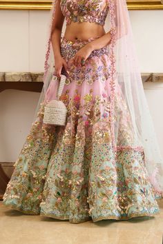 A 3-piece bridal lehenga set in pastel pink and blue, embroidered with botanical motifs and embellished with precious crystals, beads, mirror, sequins, and sea-shell detailing, creates an absolutely modern regal look. Evoking a summer and princess vibe, the set features a floor-length lehenga skirt adorned with floral embroidery, detailed with sea-shell detailing and sparks of crystals and beads. This look is completed with a shaded tulle blue and pink dupatta. Cap-sleeved designer blouse with sweetheart neckline embellished with botanical motifs. The blouse contains a left side open metal zip. The flowy translucent dupatta drenched in a pink and blue hue. Floor-length skirt adorned with hand embroidery crafting the flower motifs with the use of sea-shells, crystals, beads, and sequins. Le Multicolor Hand Embellished Sets For Reception, Multicolor Hand Embellished Lehenga For Reception, Multicolor Hand Embellished Dress For Reception, Festive Multicolor Hand Embellished Lehenga, Hand Embellished Multicolor Dress For Reception, Festive Hand Embellished Multicolor Lehenga, Wedding Lehenga Hand Embellished In Multicolor, Pink Hand Embellished Organza Lehenga, Embellished Multicolor Embroidered Sharara For Designer Wear