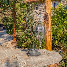 an old fashioned lamp is sitting on top of a rock in the middle of a garden