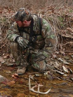 a man kneeling down next to a body of water with a deer antler in it