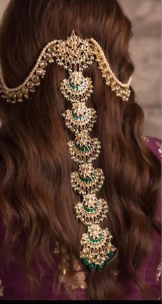 the back of a woman's head wearing a gold and green bridal hair piece