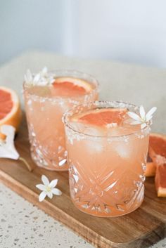 two grapefruit cocktails on a cutting board with flowers