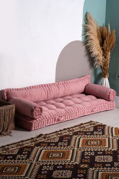 a pink couch sitting on top of a rug next to a vase filled with dry grass