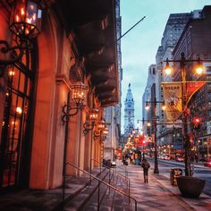 a city street at dusk with people walking on the sidewalk and buildings in the background