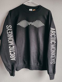 a black sweatshirt with white letters on it hanging from a hanger against a wall