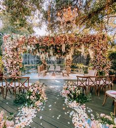 an outdoor ceremony setup with flowers and chandelier hanging from the ceiling, surrounded by greenery