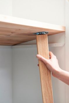 a hand is holding the edge of a wooden shelf