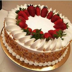 a white cake with strawberries on top is sitting on a gold platter and sits on a table