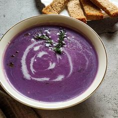 a bowl of purple soup next to slices of bread